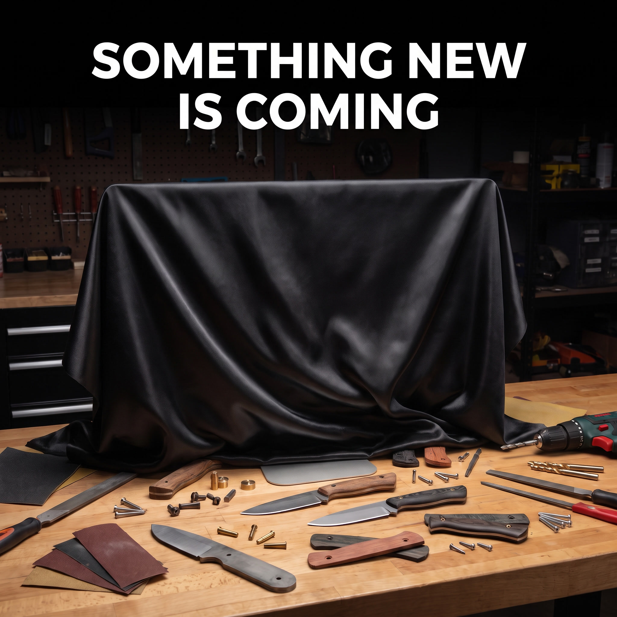 Workbench with knives and knifemaking tools and a rectangular object draped with a black satin cloth and text that reads “Something New Is Coming“