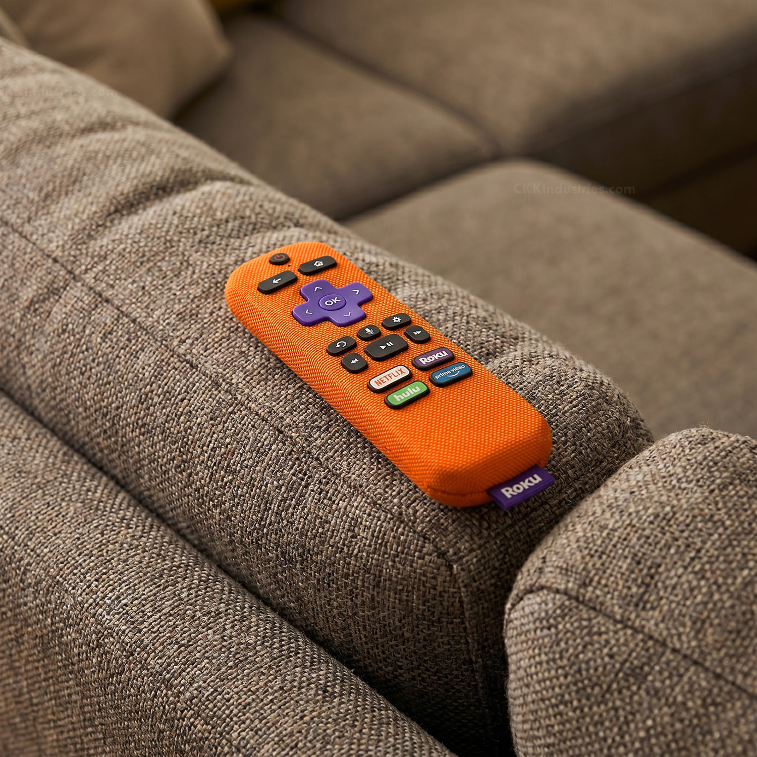 A tv remote wrapped in Blaze Orange EDC Wrap laying on the back of a brown sofa