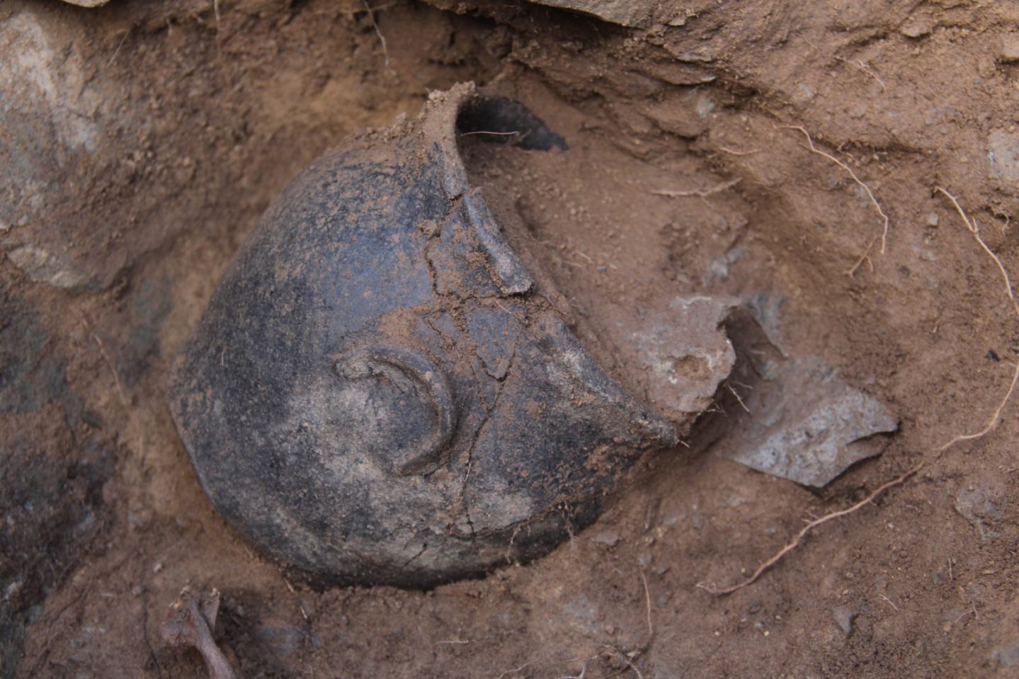 A close-up photograph of an ancient ceramic pot half-buried in the ground.