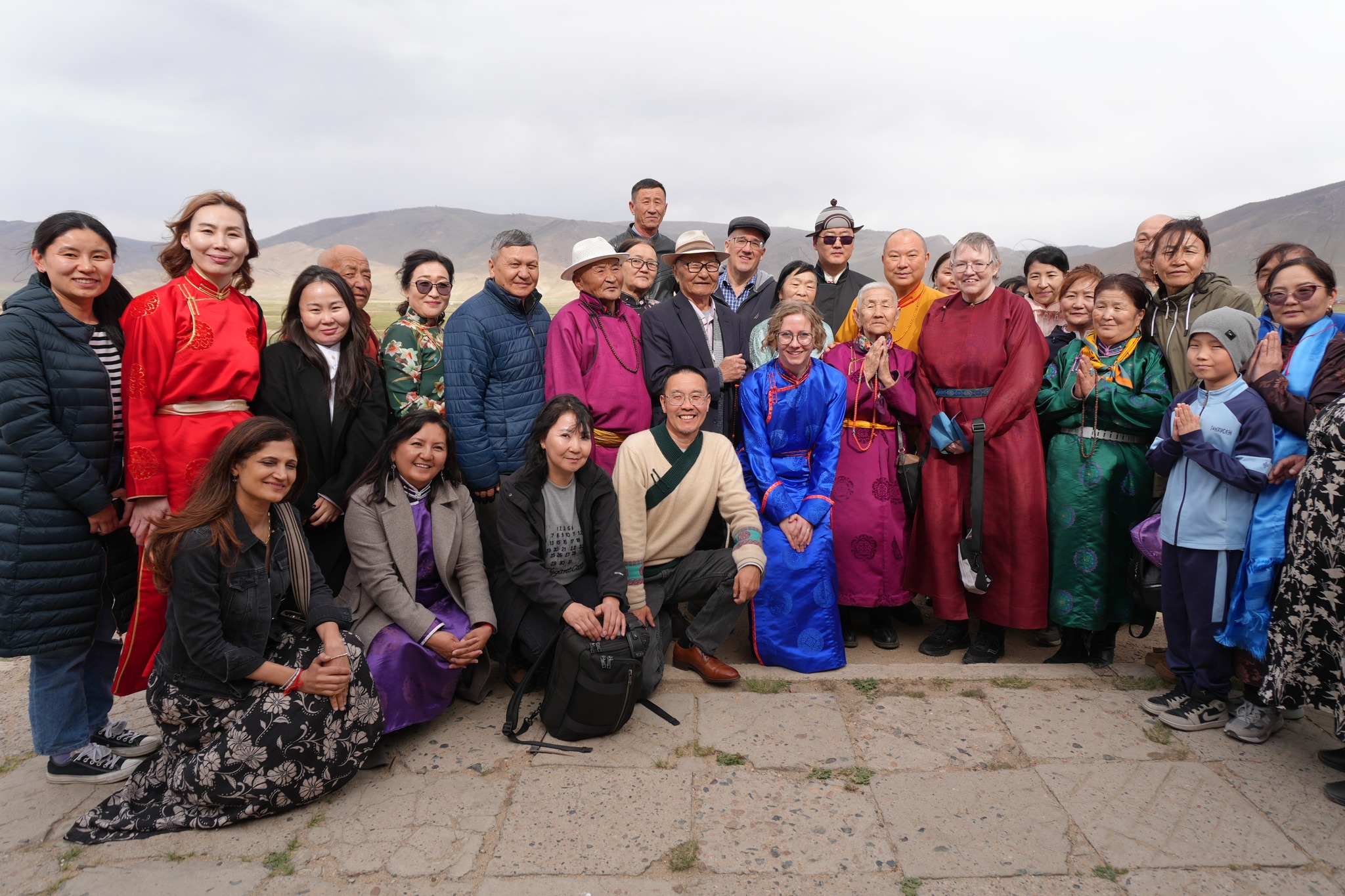 A group of men and women standing outside on a hilltop smiling at the camera.