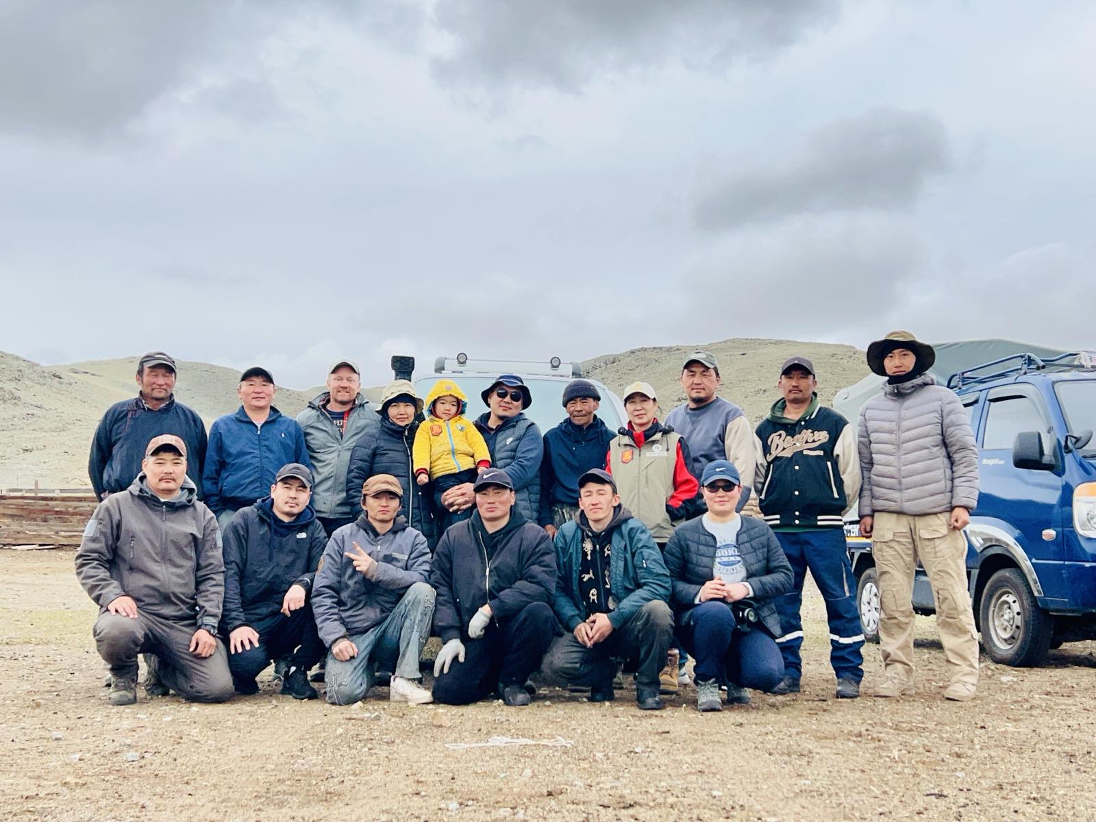 A group of archaeologists post outside on the steppe in front of their vehicles.