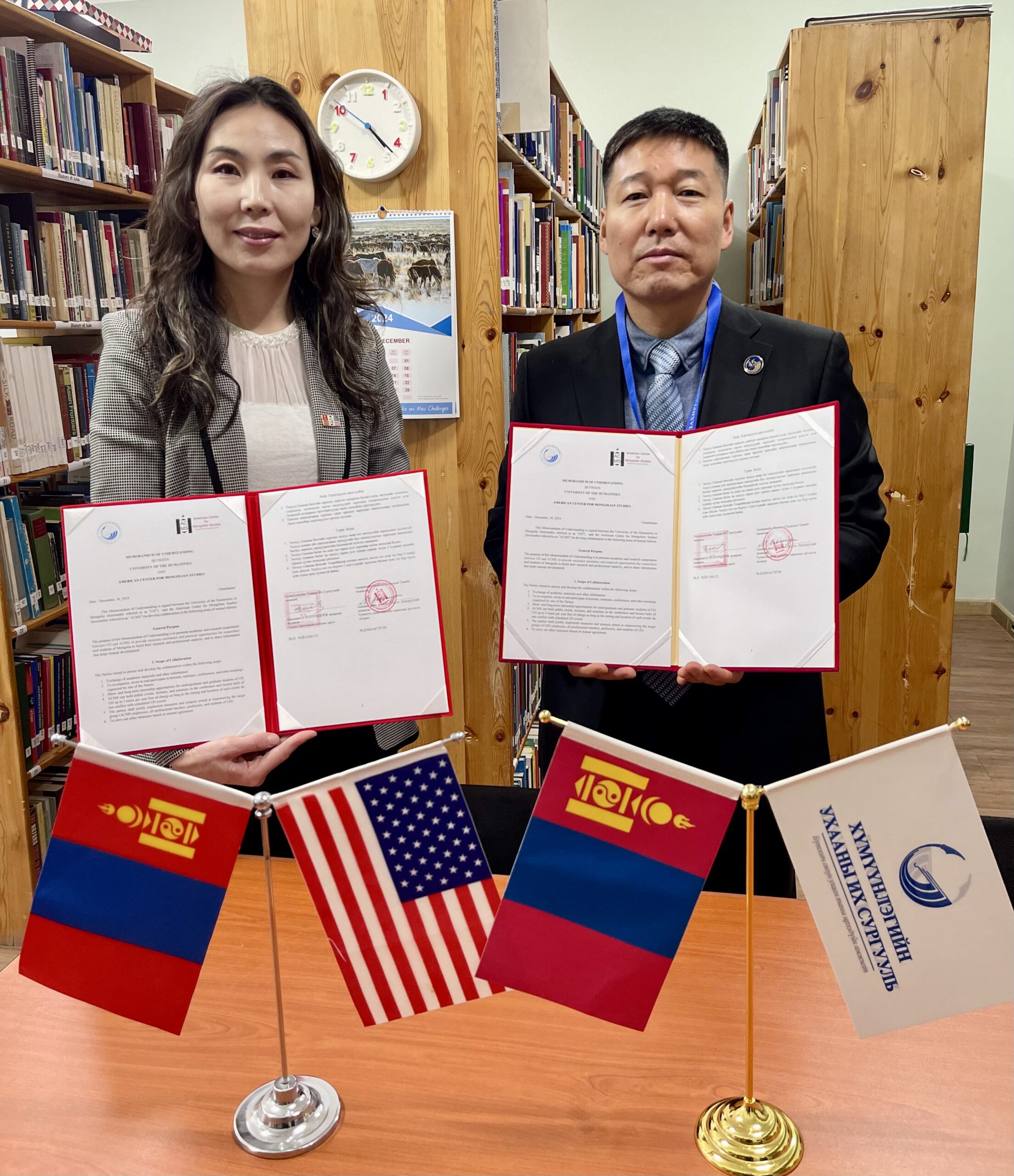 A man and a woman stand behind a desk and display copies of a newly-signed document.