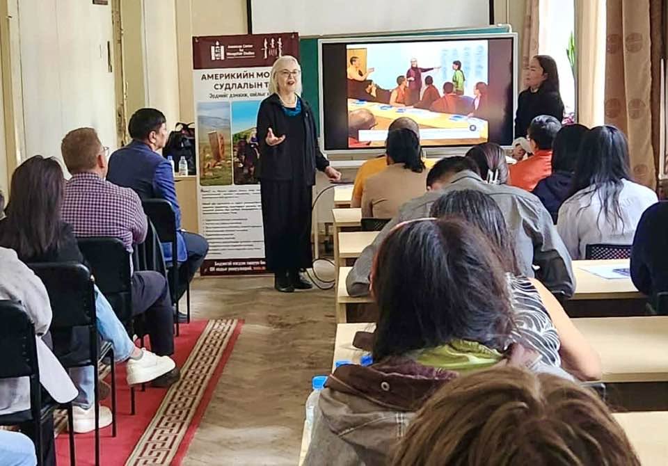 A picture of an older American woman giving a presentation to a group of Mongolian students, conservators, and enthusiasts focused on conservation.