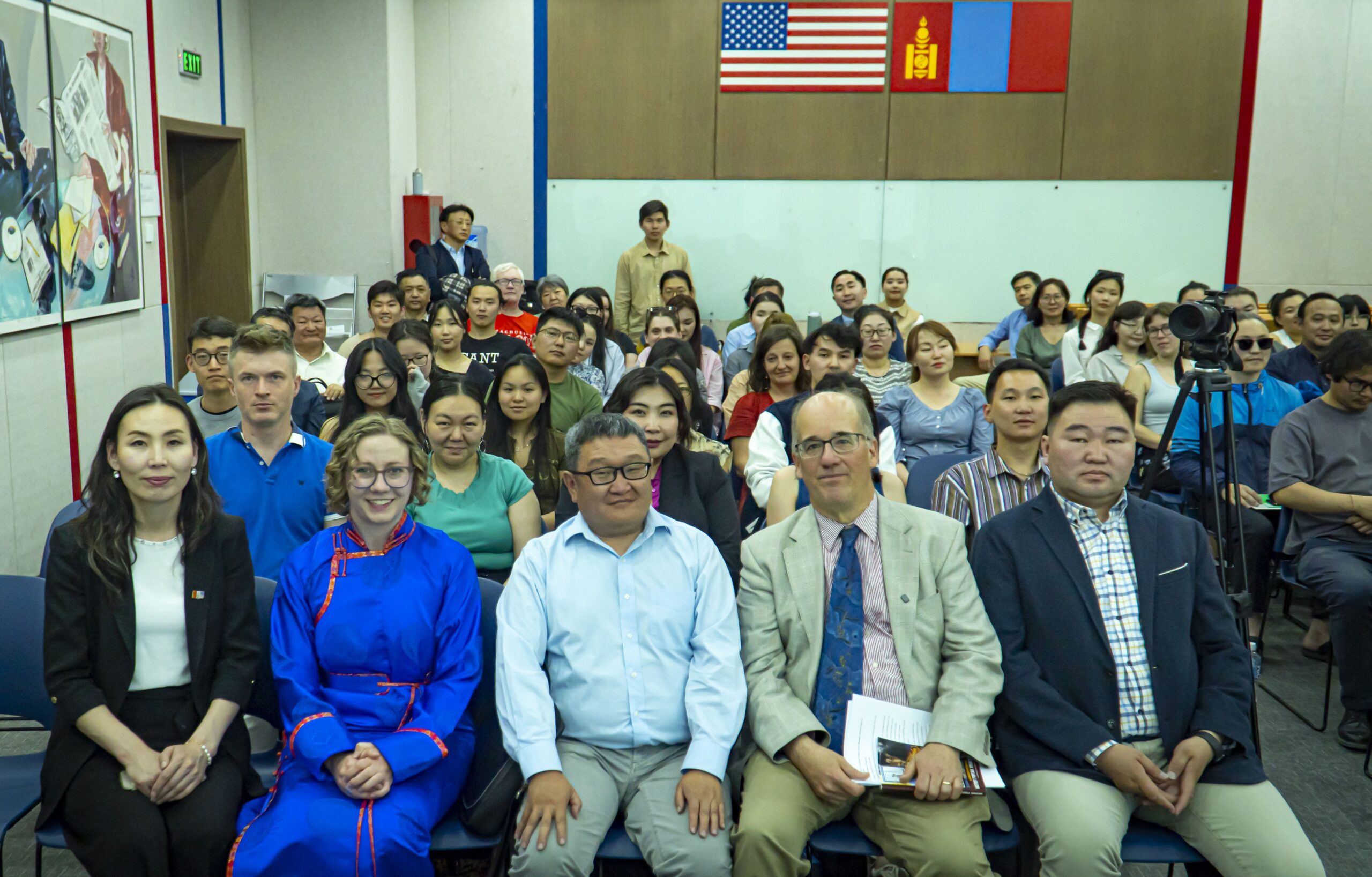 A group of people sitting in rows in an auditorium looking at the camera and smiling