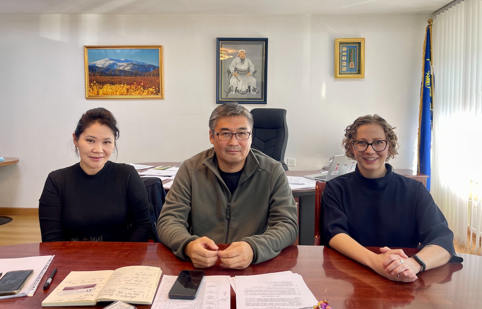 Three people sitting at a table with papers laid out in front of them. Far left: Dr. Munkhtogoo Dulamjav. Middle: Dr. Enkhbat Galbadrakh. Far right: Maggie Lindrooth 