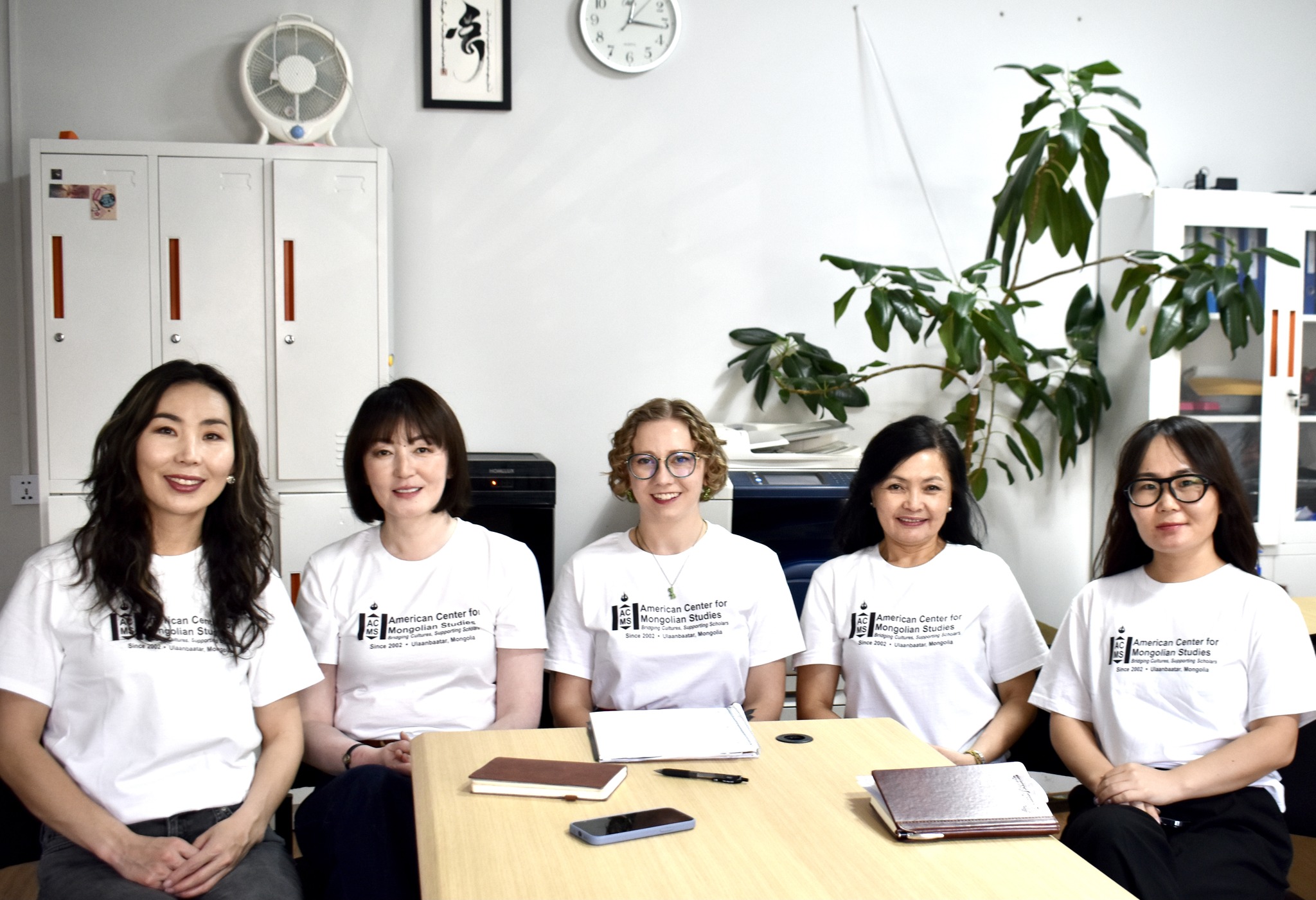 Five women seated around a table wearing matching shirts that read “American Center for Mongolian Studies.“ From left to right: M. Davaasuren, B. Baigalmaa, Maggie Lindrooth, T. Tsermaa, T. Tuvshinzaya