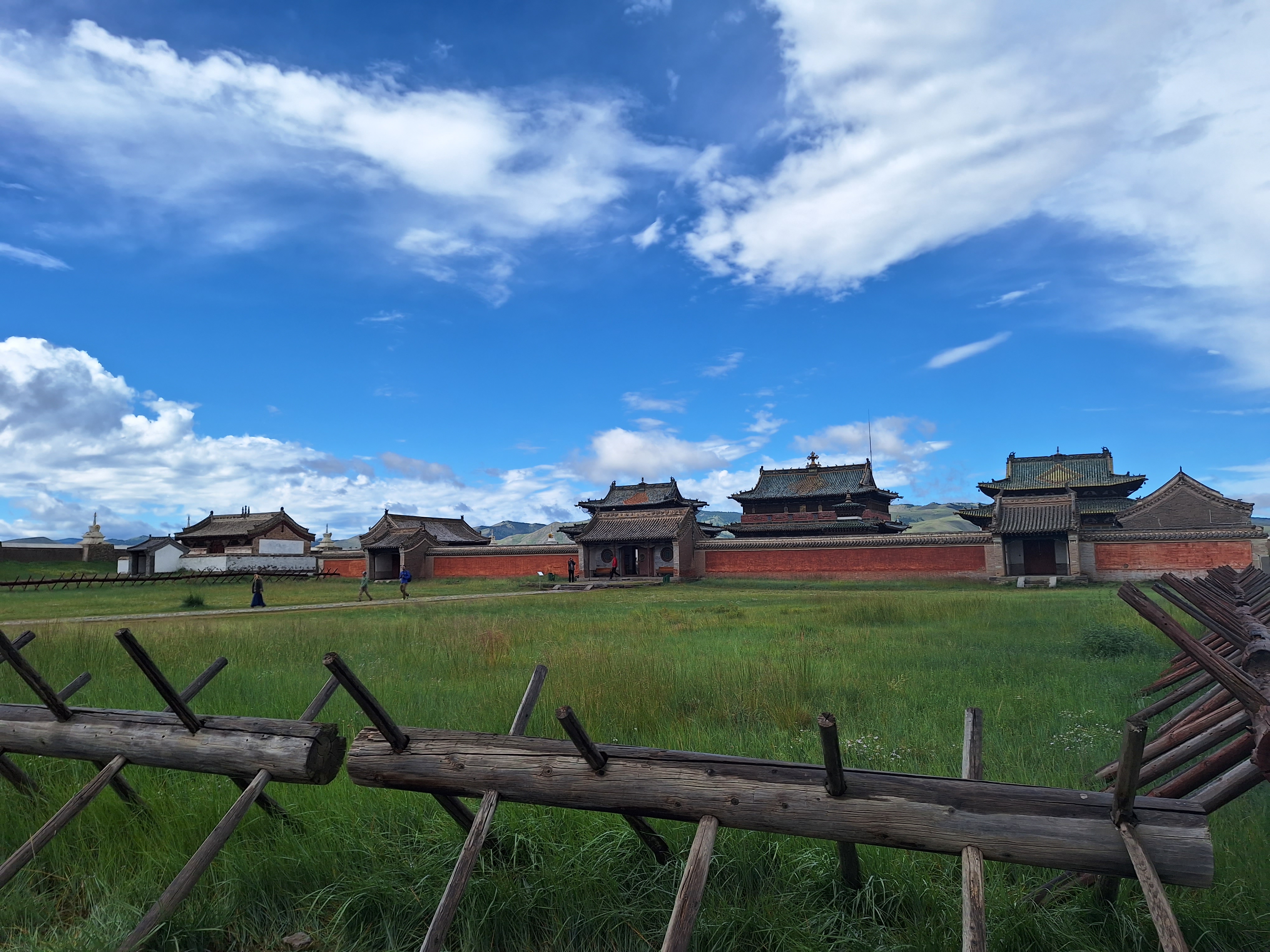 A monastery located in the Mongolian countryside. People are walking out of the entrance. A blue sky full of clouds hangs above.