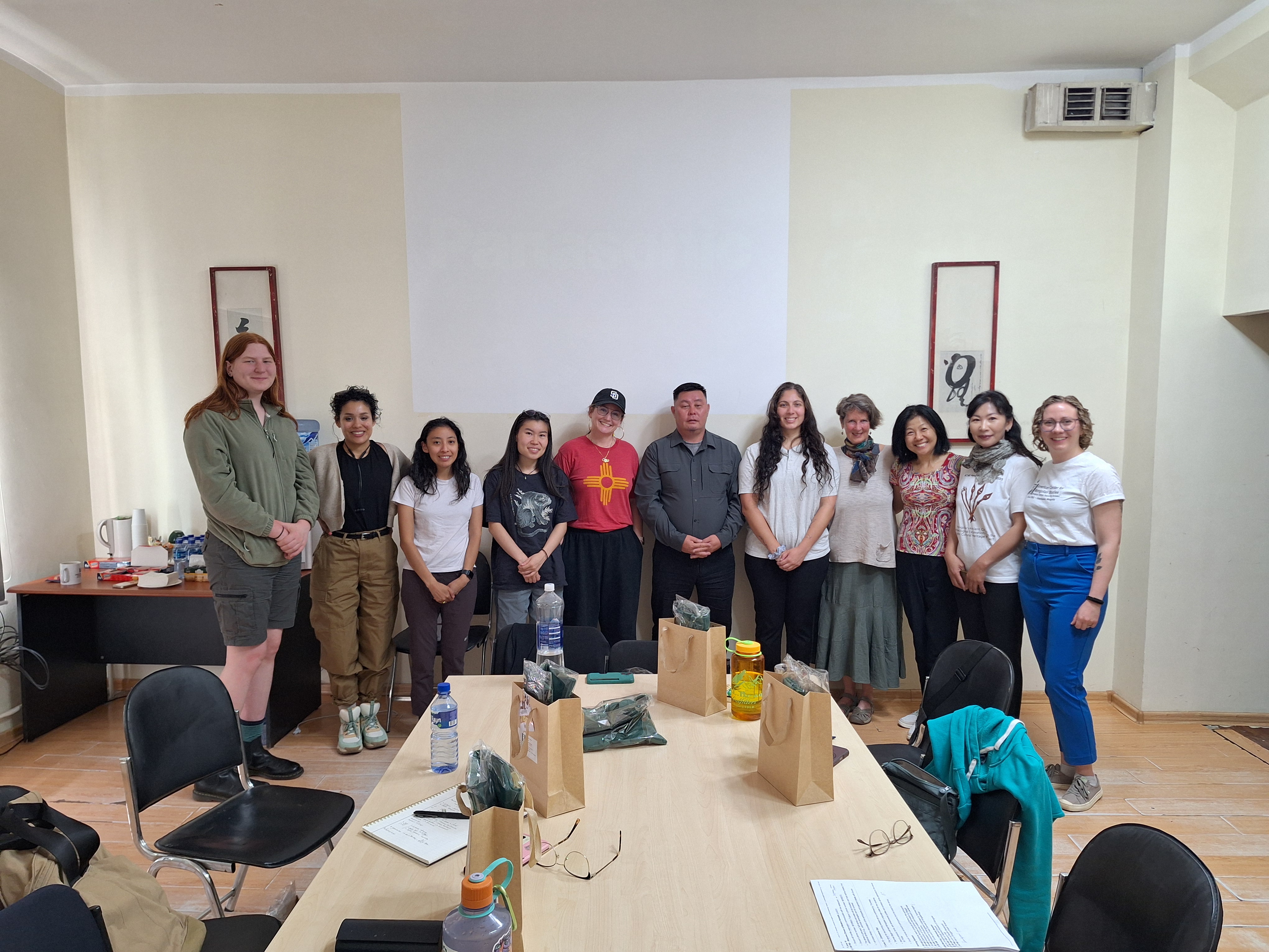 A group of people standing in a line in a classroom smiling at the camera
