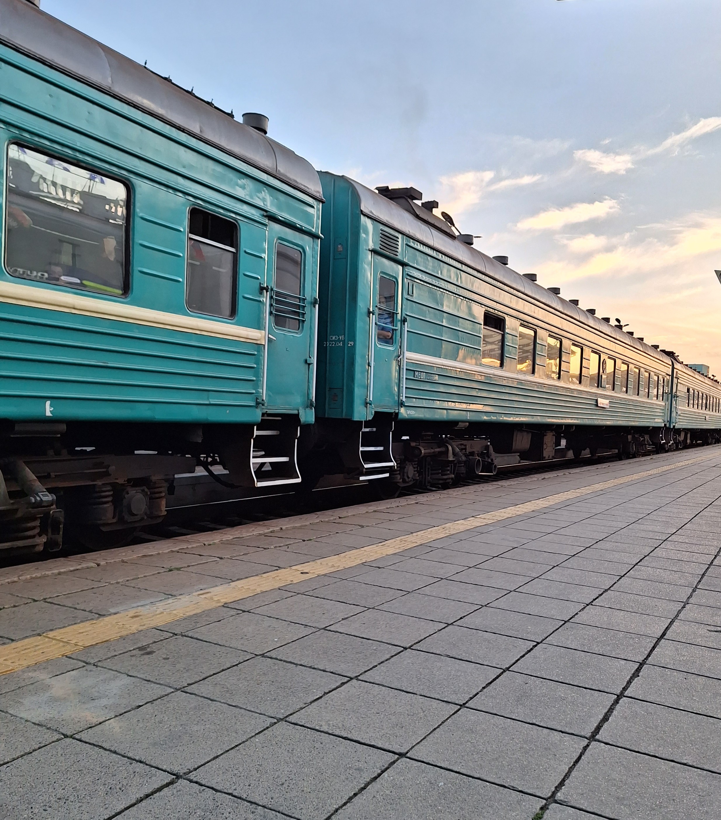 Green train cars stand at a train station platform.