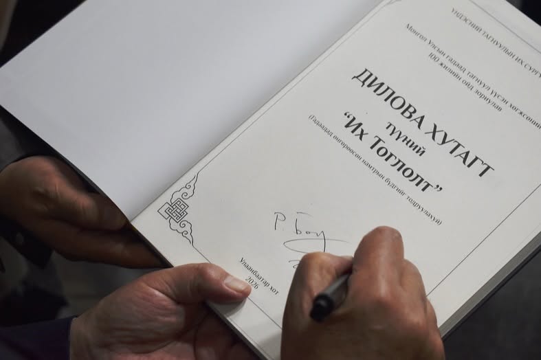 A close-up picture of a hand signing the title page of a book that says, in Mongolian cyrillic script, “the Dilowa Hutughtu and his 'Great Game.'“