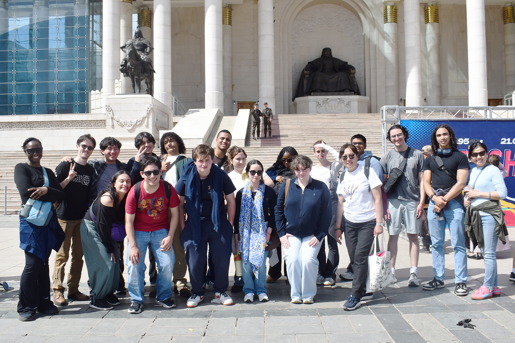 A group of American high school students stands in front of a large white marble building with a large statue of Genghis Khan behind them.