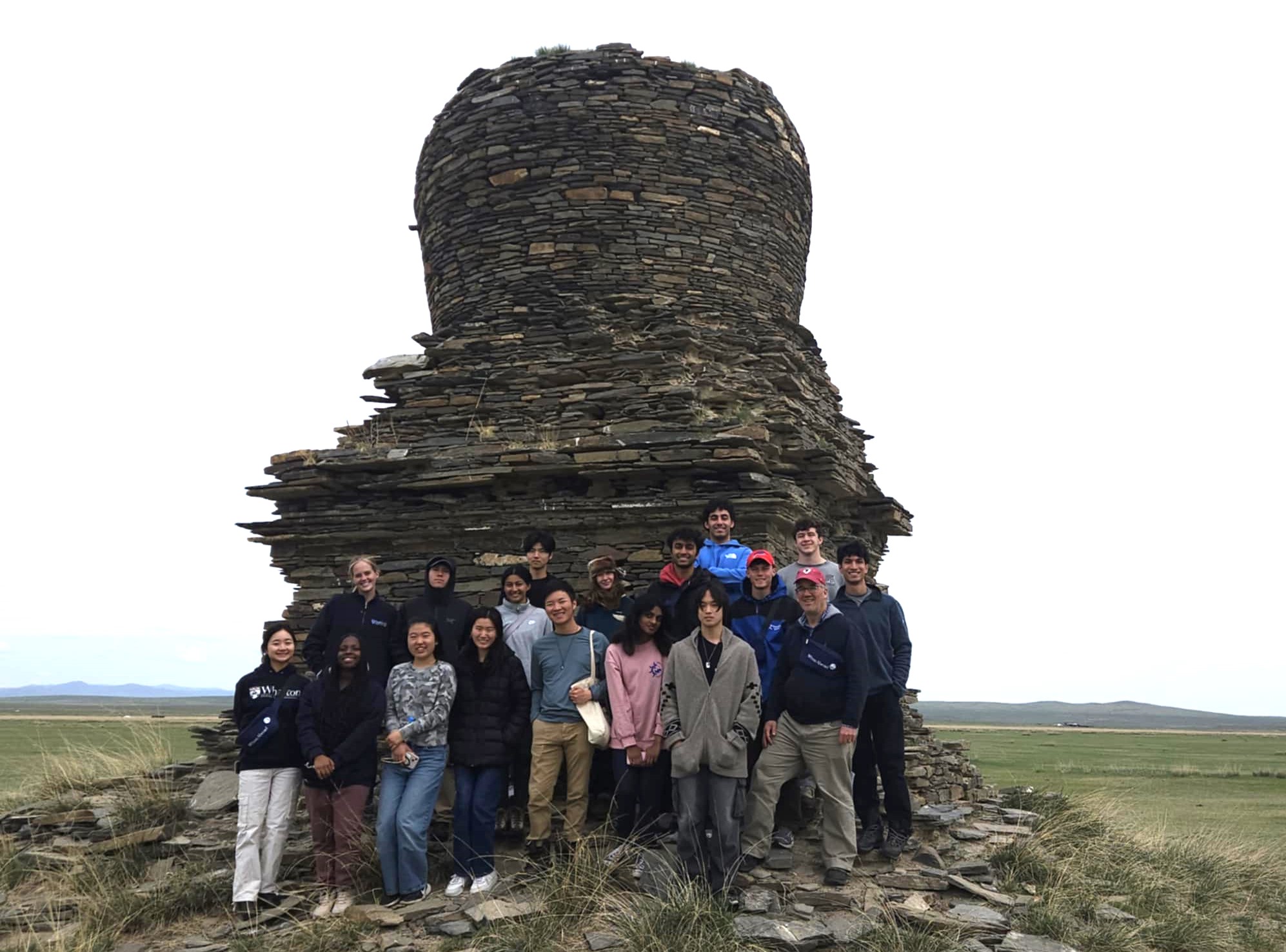 A group of undergraduate students standing with their professor in front of an ancient architectural ruin in the Mongolian countryside