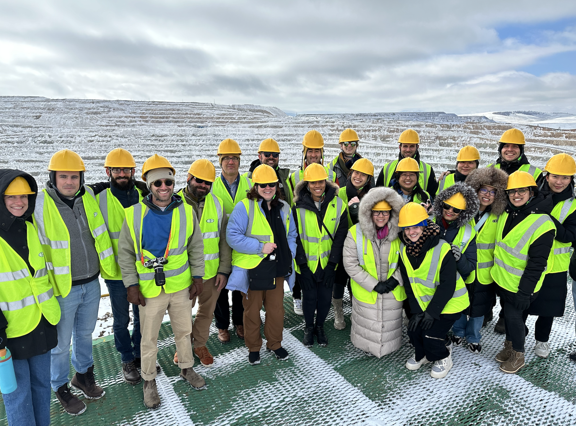 A group of students in neon yellow safety vests and hard hats standing on the edge of a snow-covered pit mine.