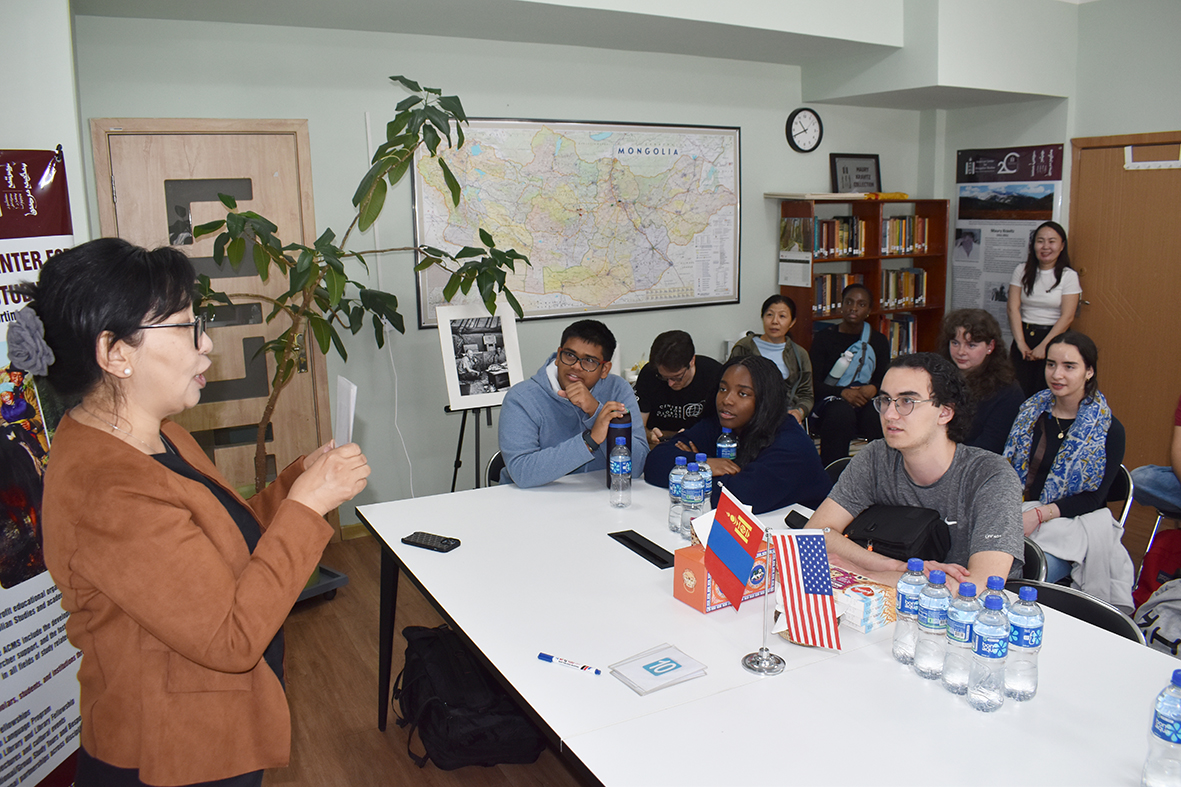 A group of young people sit and pay attention to an adult woman giving a presentation.