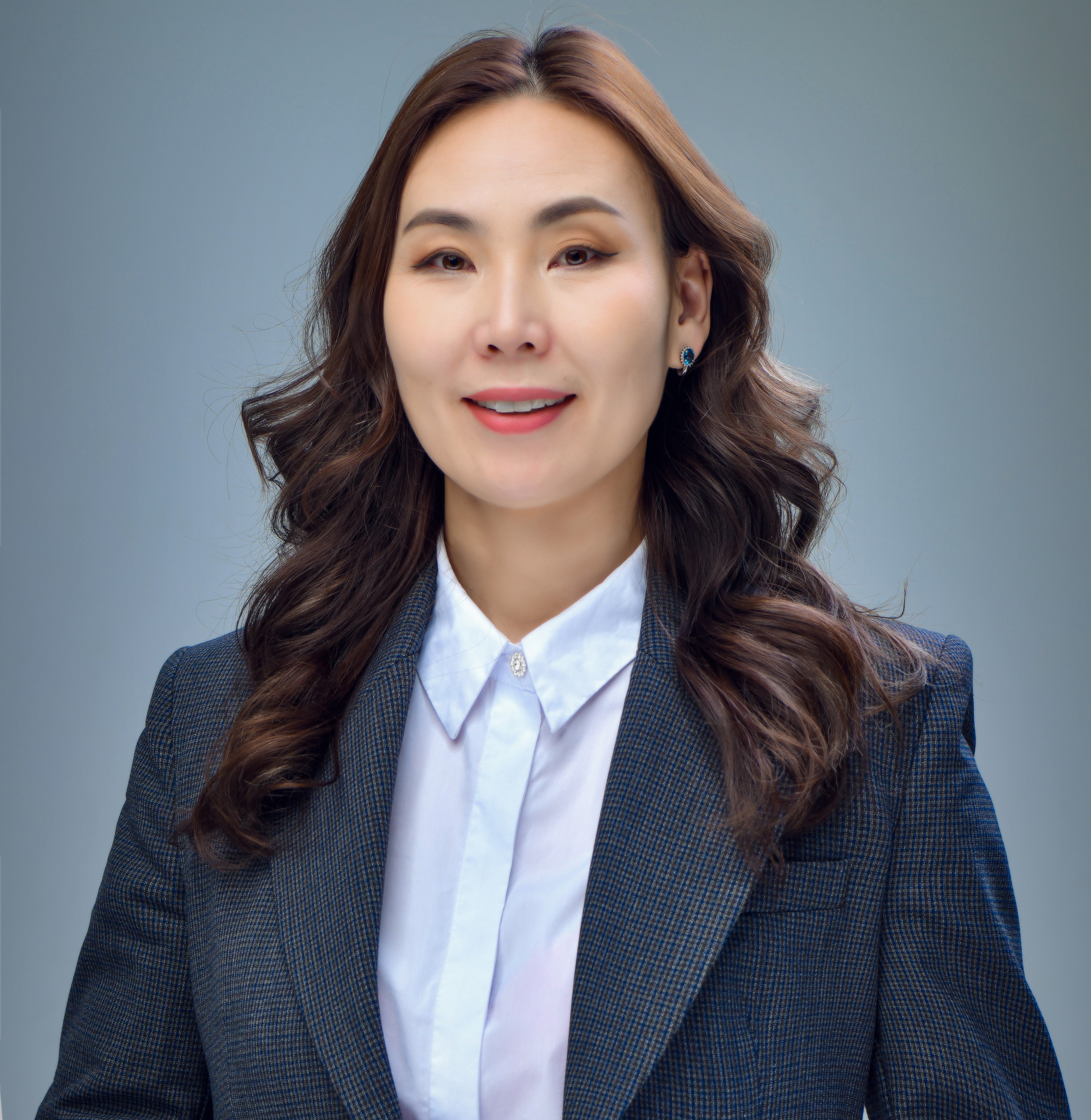 A close-up photo of a Mongolian woman in a charcoal gray blazer and a white button-down shirt smiling and looking at the camera.