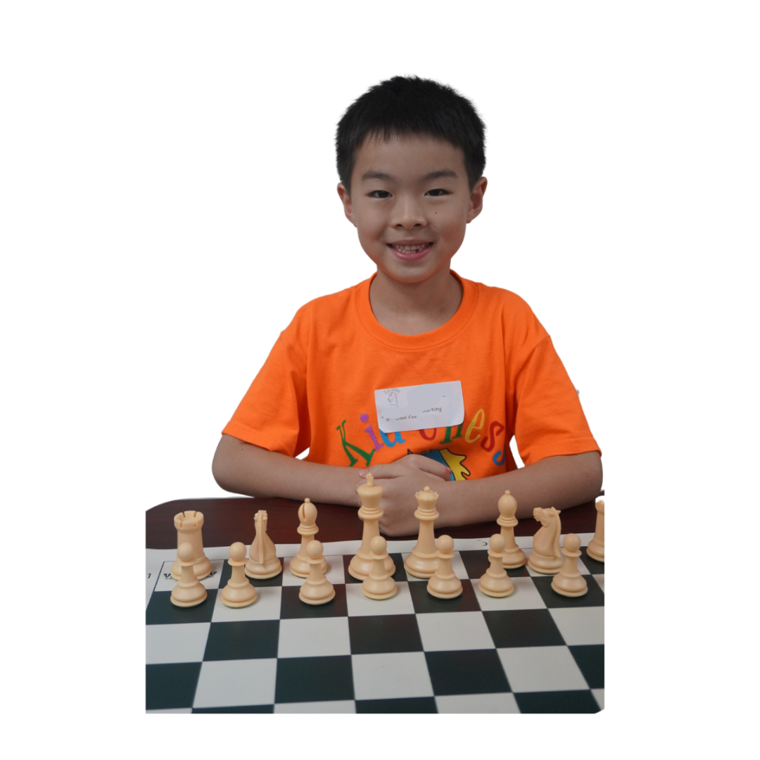 Boy in an orange shirt smiling over a chess board