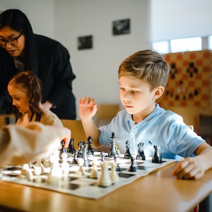 A picture of a child thinking inquisitively about his next move on the chess board. 