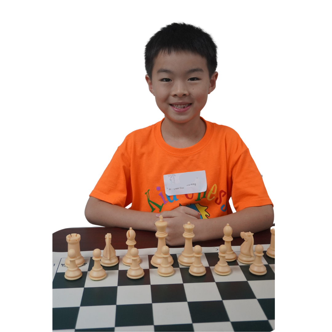 Boy in an orange shirt smiling over a chess board