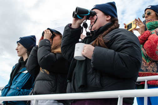 People in coats and hats use binoculars to search for wildlife aboard Swiftsure. 