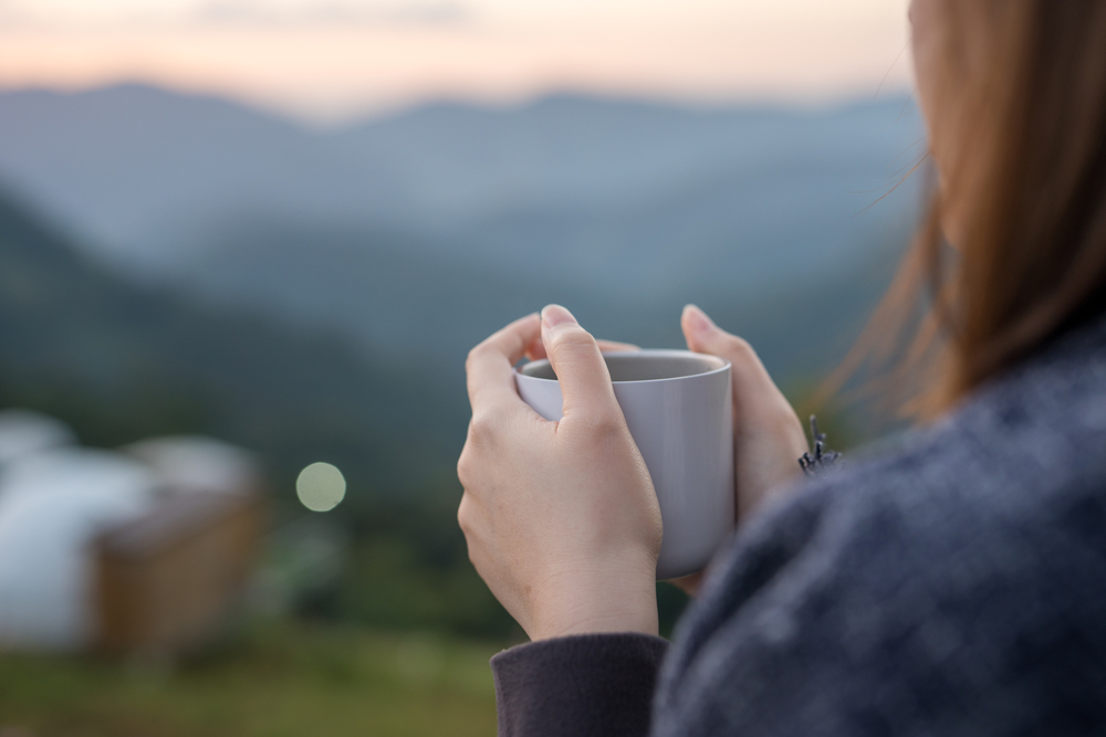 Woman looking off into a mountainous view while holding a coffee cup.
