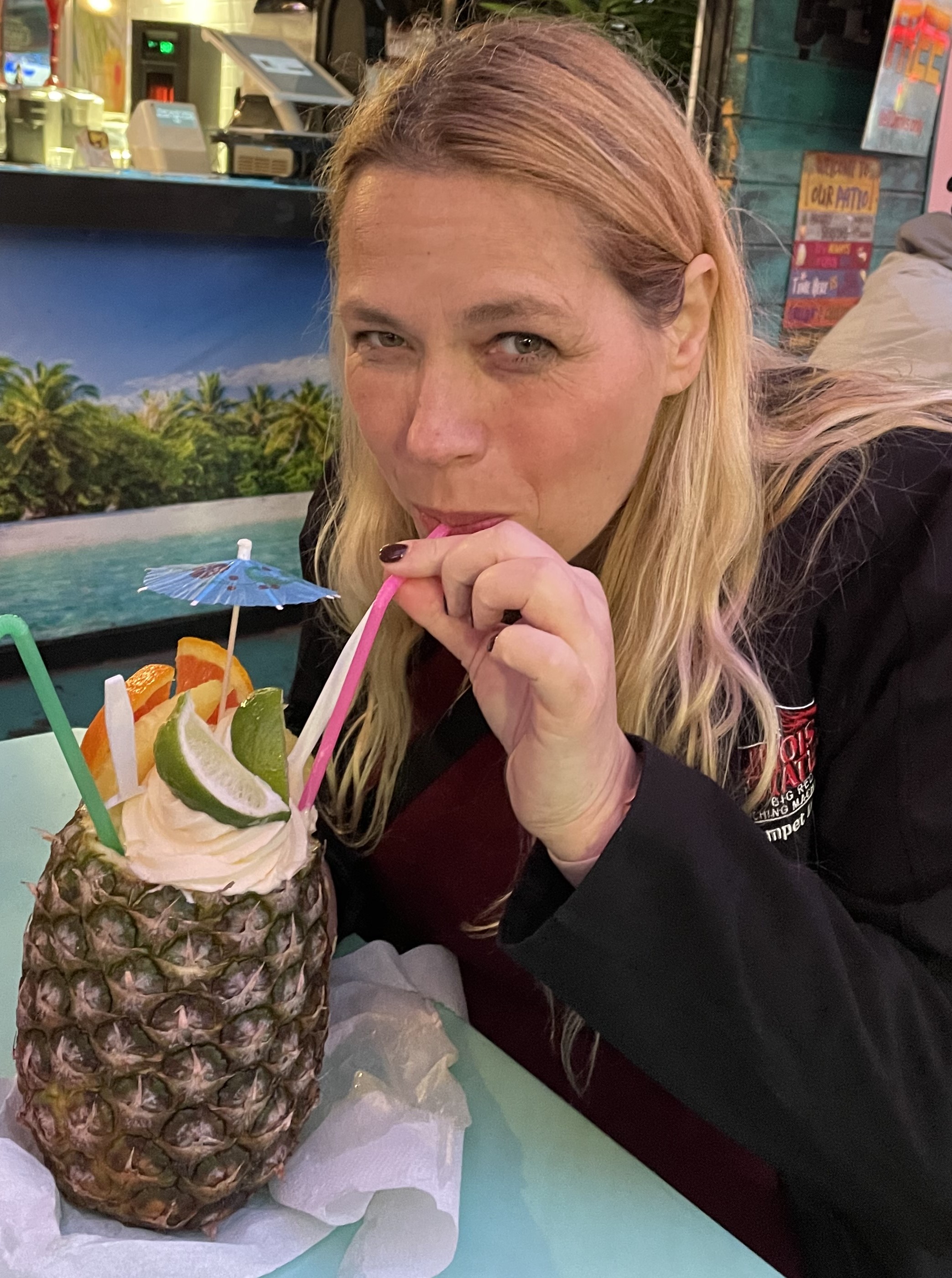 Mari smiling at the camera while drinking a fruity ice cream drink from a pineapple.