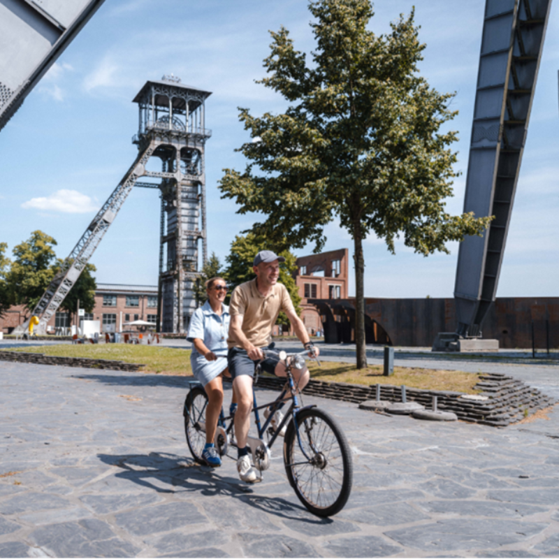 twee mensen op een fiets met een schachtbok op de achtergrond