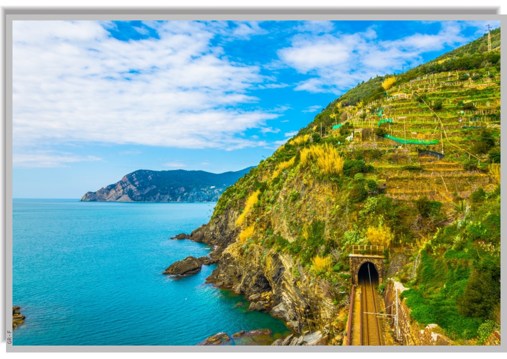 A green cultivated hill overlooking the sea, with a coastal railway that enters a tunnel in the hill