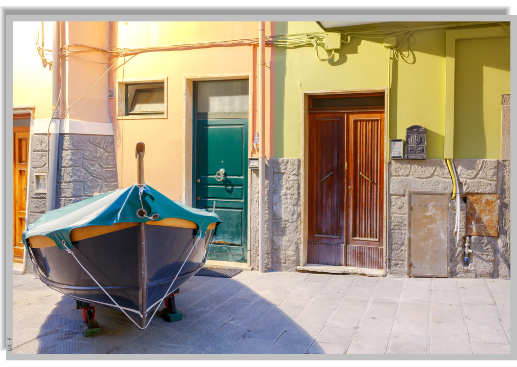 A "gozzo", the typical ligurian little boat, pulled up and parked on the paved street in front of a colourful house