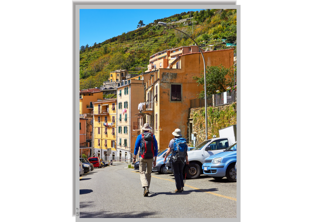 Two hikers with their backpacks walking along a street in Riomaggiore in a sunny day