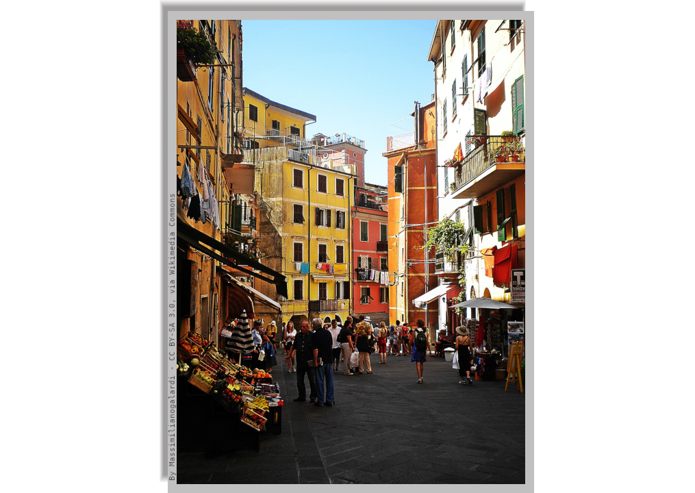 An internal street of Riomaggiore lined with colorful houses and populated by locals and tourists who stroll through the shops