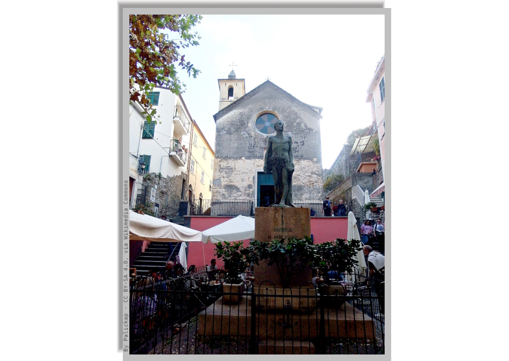 Monument in a square and, in the backgroung, the facade of the church of the village