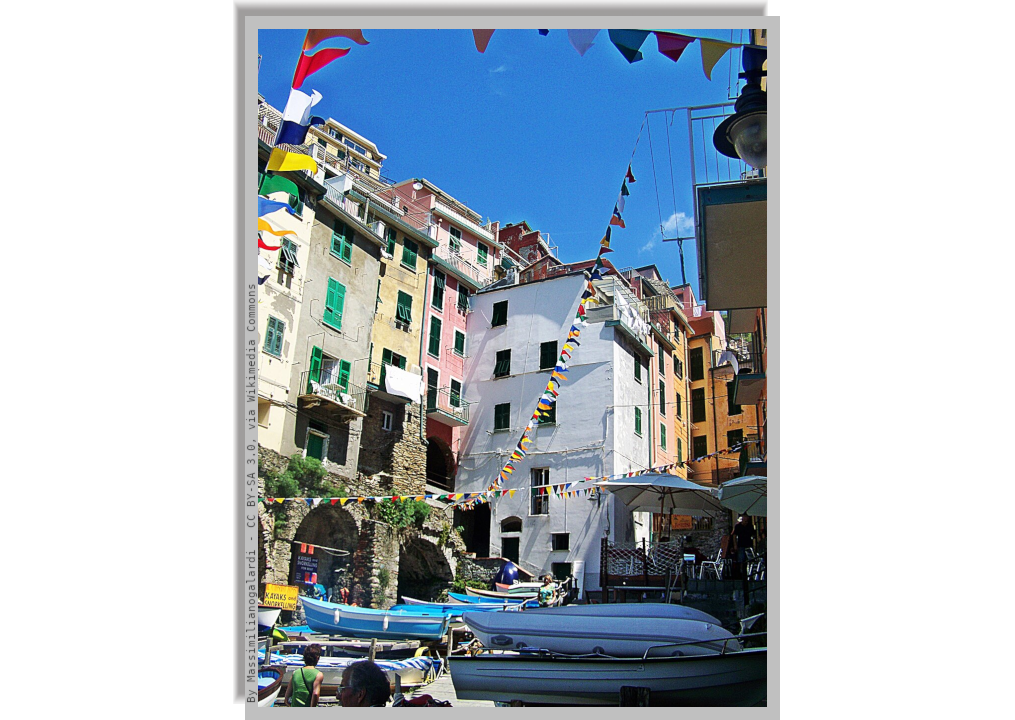 Suggestive view of the houses of Riomaggiore, and in the space among them, a square where some gozzi (little boats) are pulled up, with outdoors tables and a gazebo.