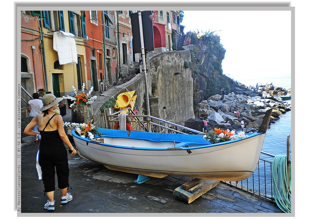 A "gozzo", the typical ligurian little boat pulled up and parked onto a street by the sea, surrounded by the colorful facades of little houses