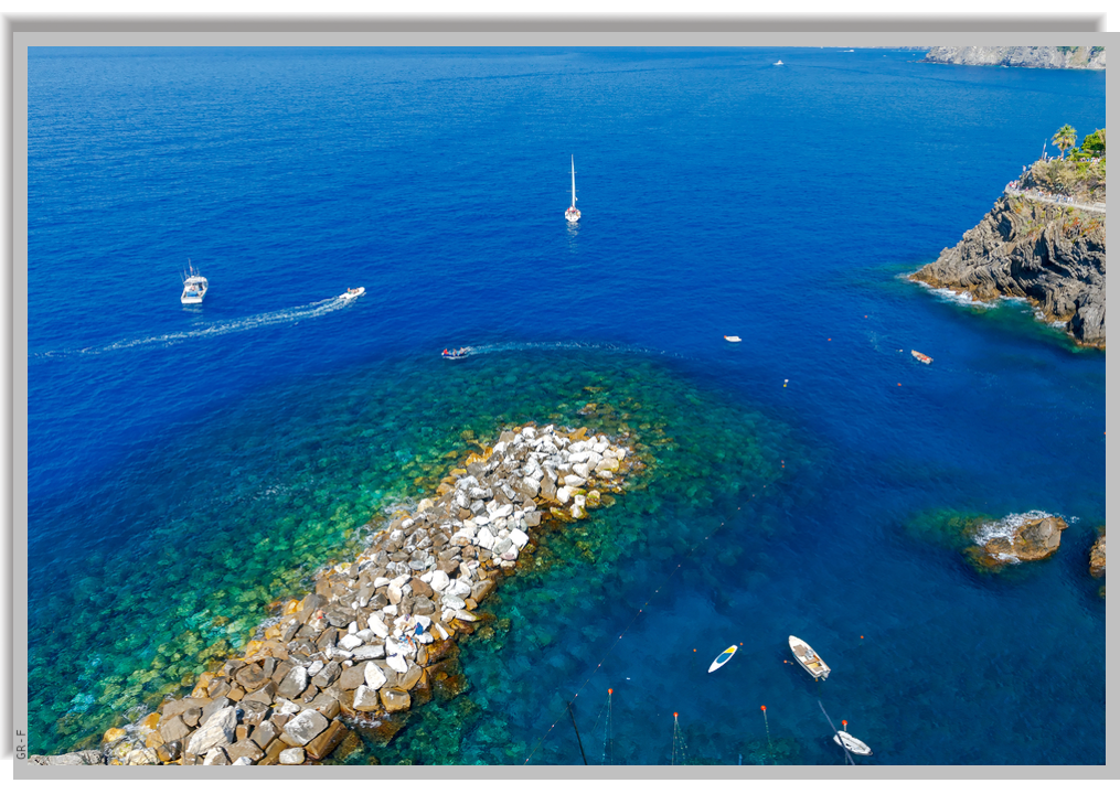 Blue calm waters and boats sailing near the cove of Manarola