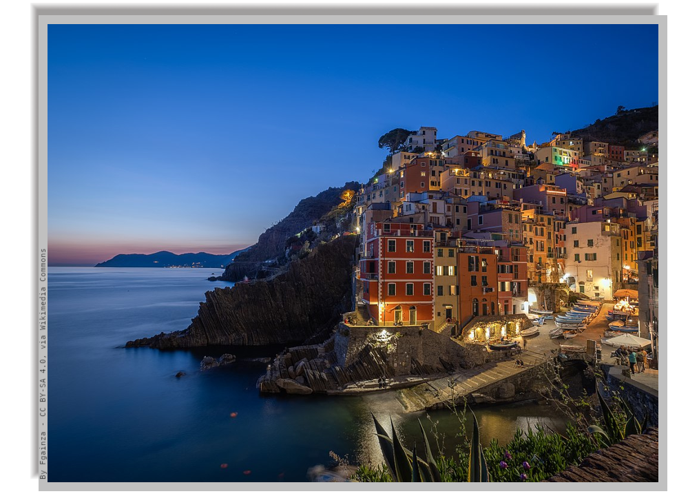 Riomaggiore illuminated in the evening and in the background the ligurian coast