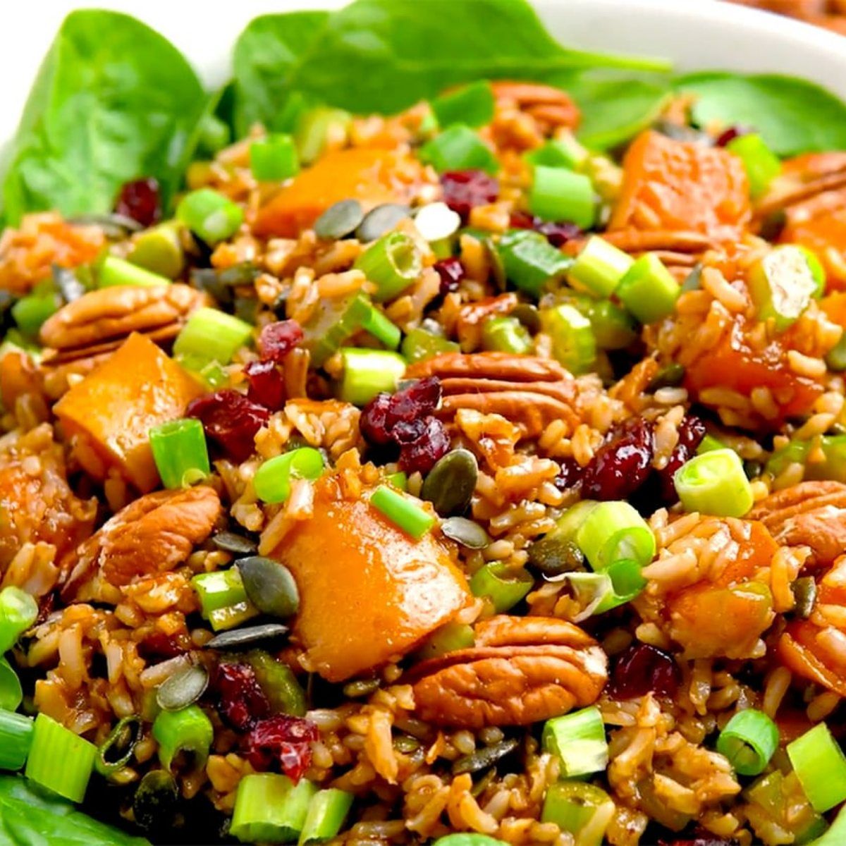 A colorful salad featuring brown rice, roasted sweet potato chunks, pecans, dried cranberries, green onions, and pumpkin seeds served over a bed of fresh spinach.