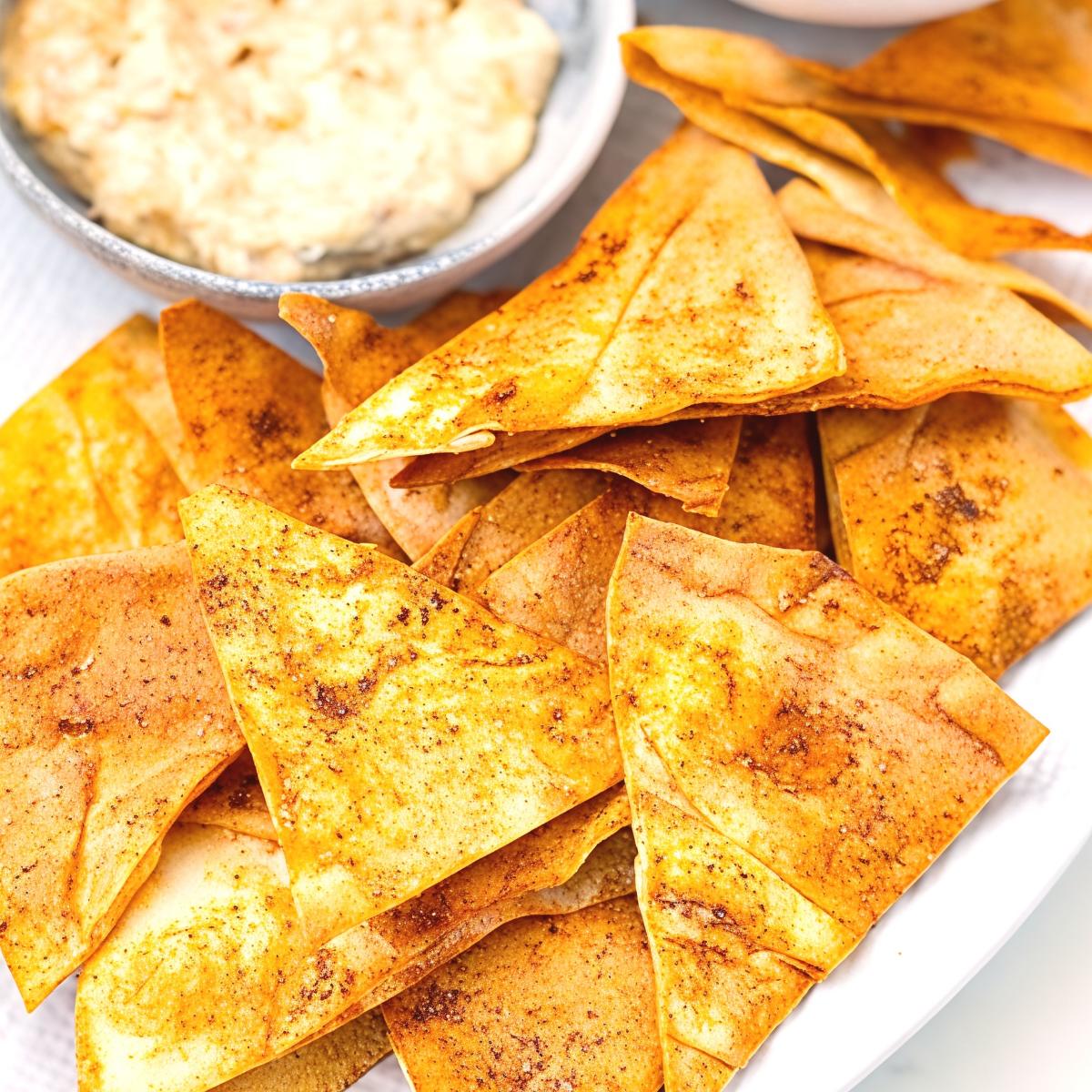Crispy homemade seasoned pita chips piled on a serving platter alongside a bowl of creamy dip, perfect for easy party appetizers.