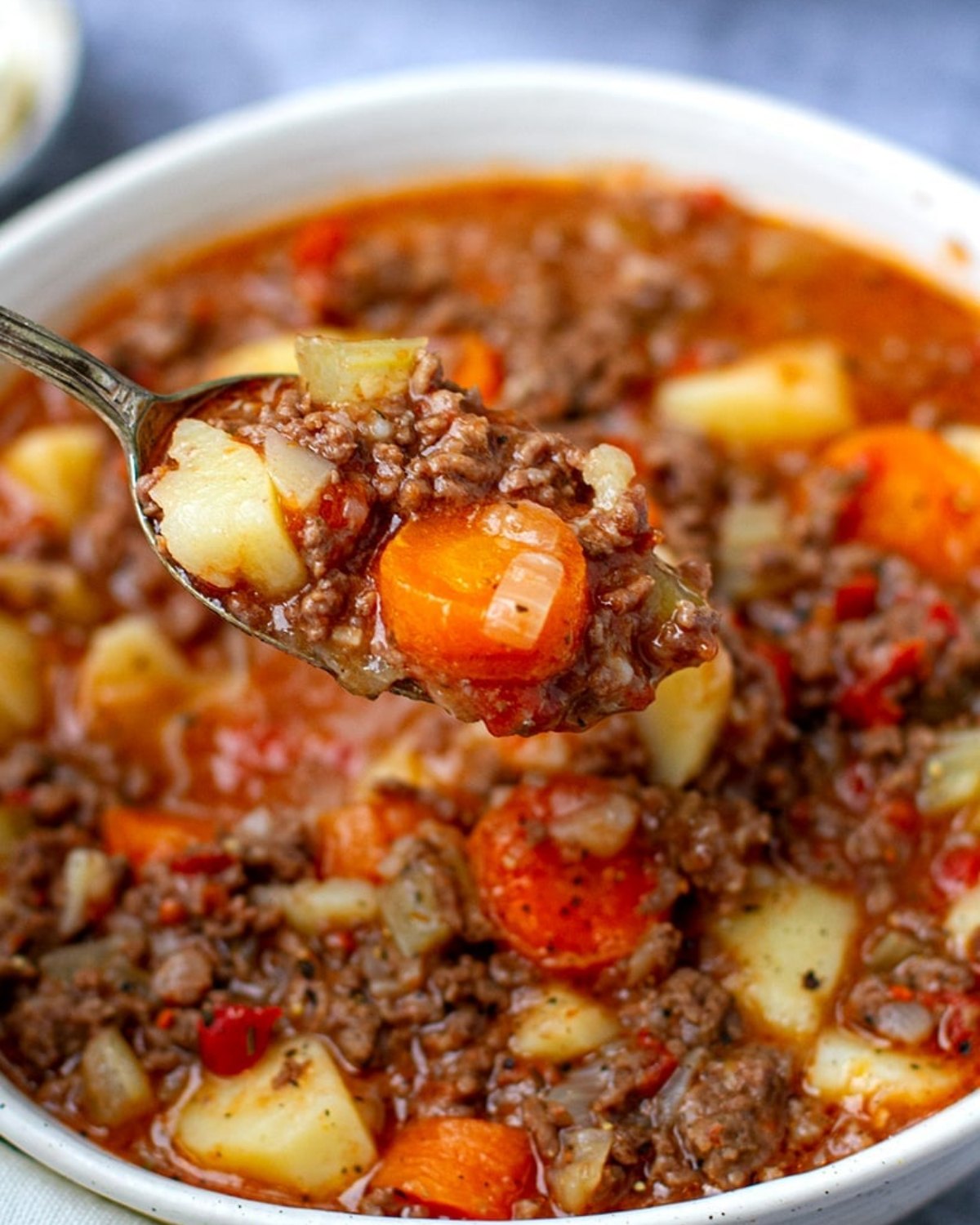 A close-up view of a comforting Instant Pot ground beef stew in a bowl, with a spoonful showcasing potatoes, carrots, and savory beef.