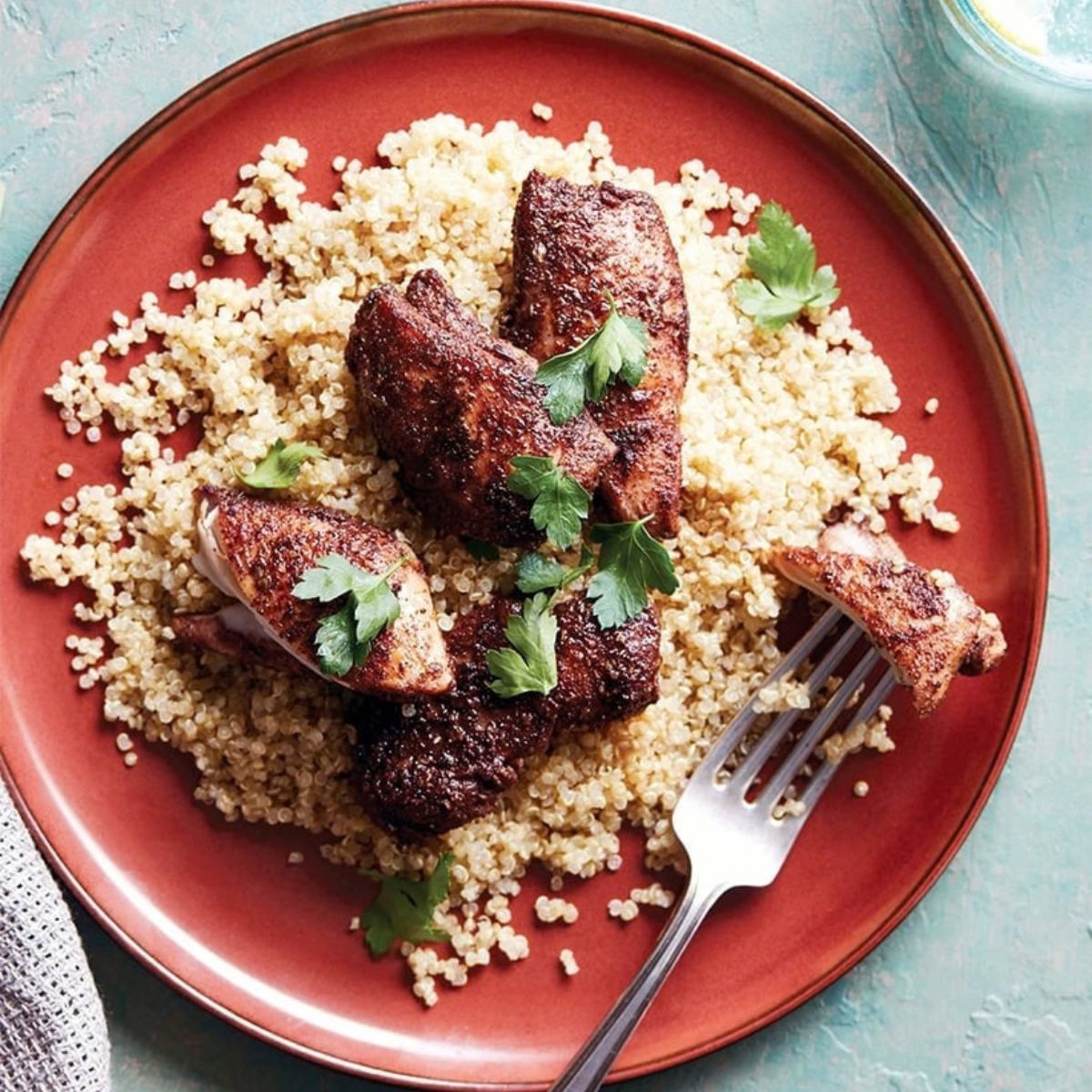 A top-down view of flavorful Instant Pot jerk chicken served over a bed of fluffy quinoa on a red plate, garnished with fresh cilantro.