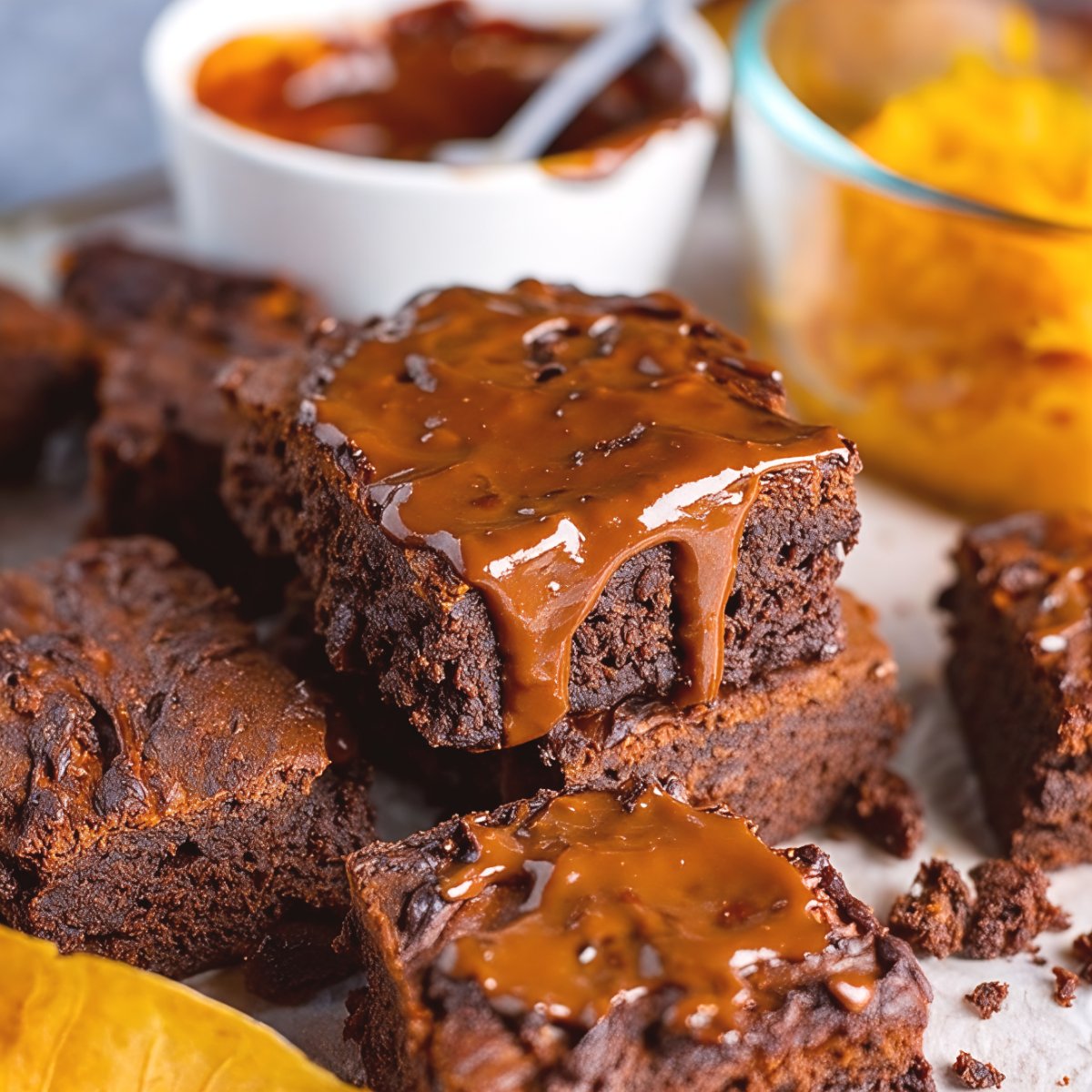 A stack of fudgy chocolate brownies drizzled with warm, glossy salted caramel sauce, serving as a rich autumn dessert platter treat.