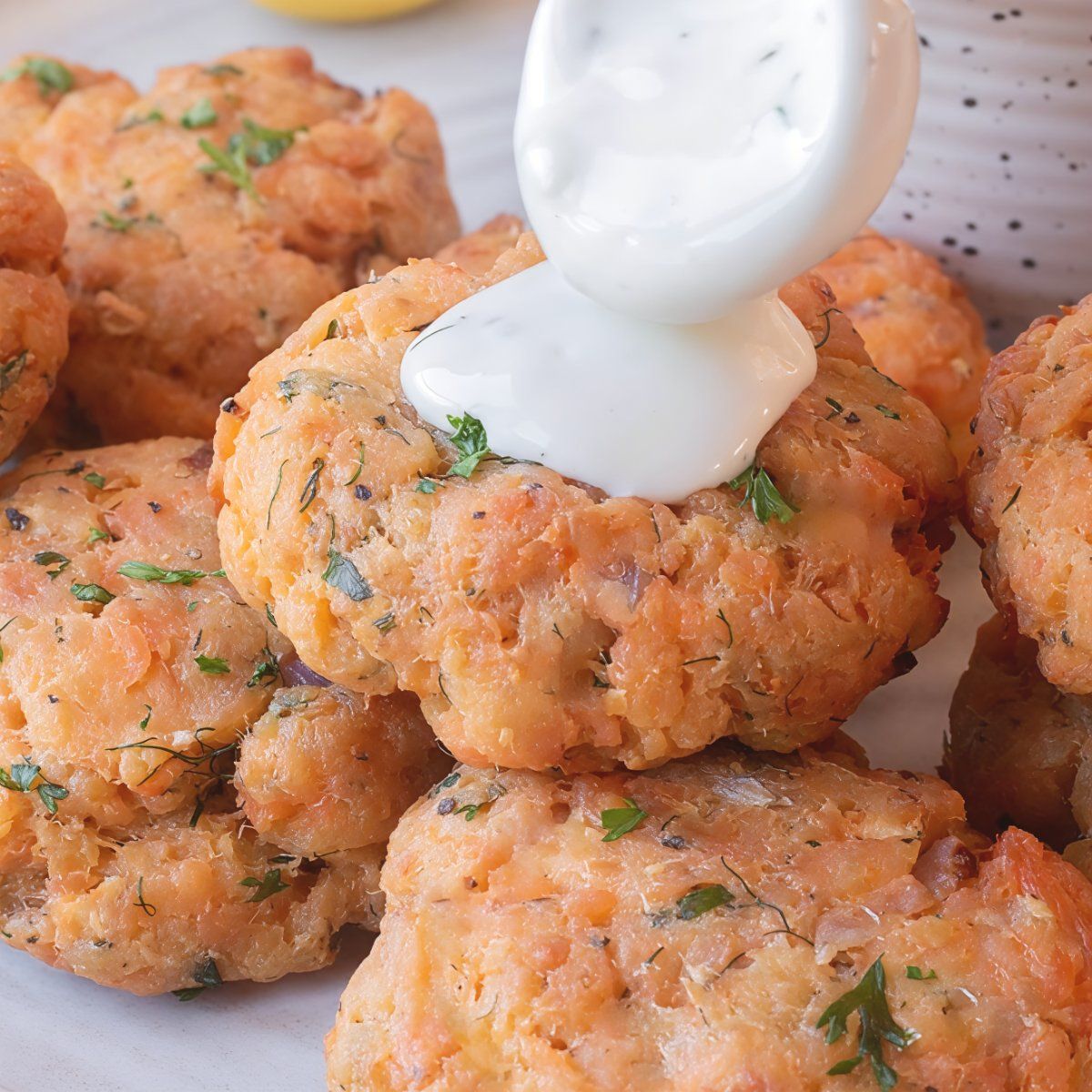 Golden crisped air fryer salmon patties garnished with fresh herbs being topped with creamy tartar sauce