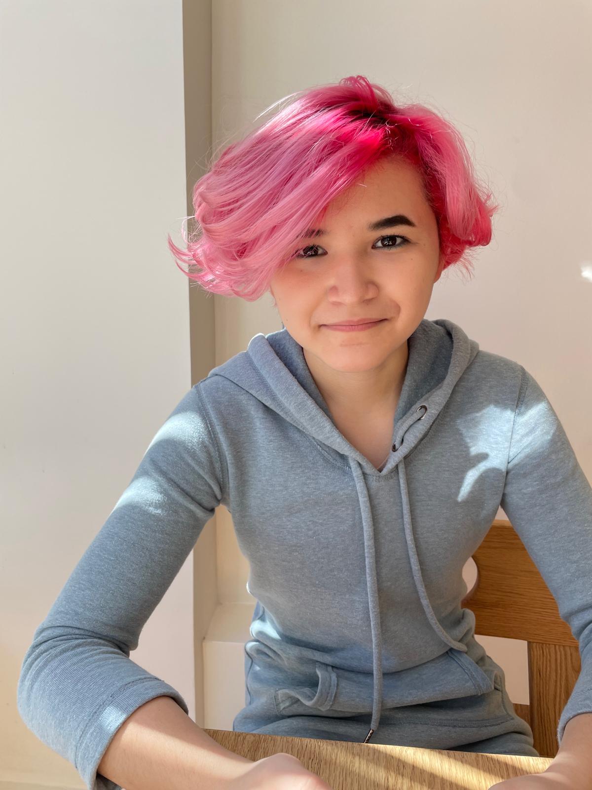 A picure of a pretty asian teenager with pink hair wearing a soft light blue hoodie