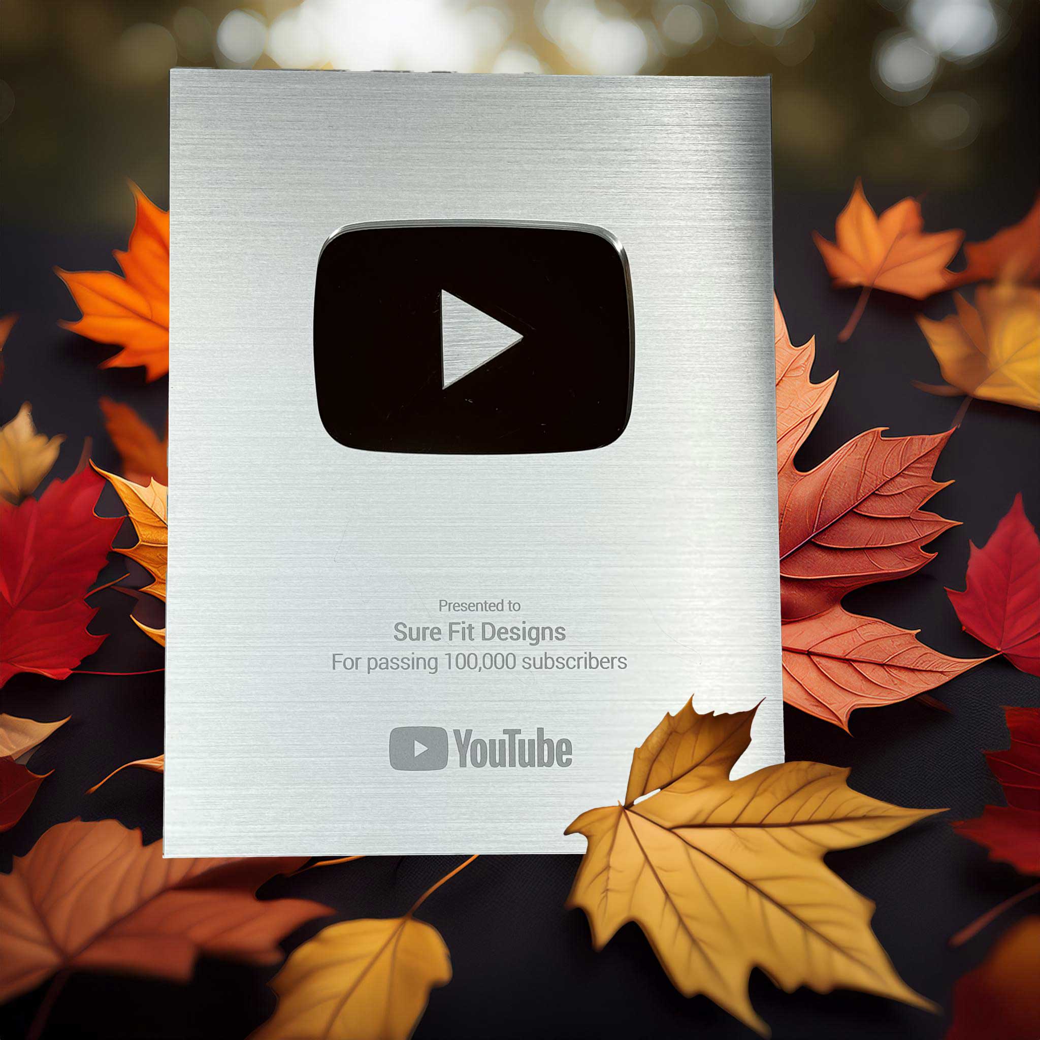 A silver YouTube plaque with fall leaves for Sure Fit Designs passing 100,000 subscribers