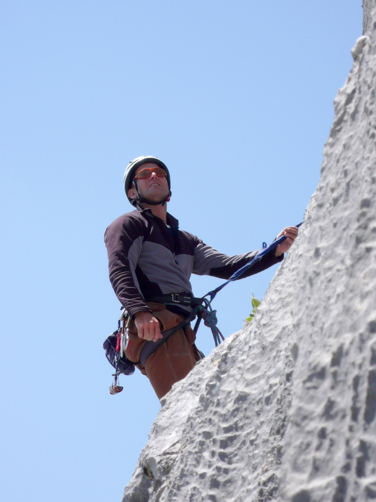 Mountain guide leading a rope climb on granite wall under clear sky