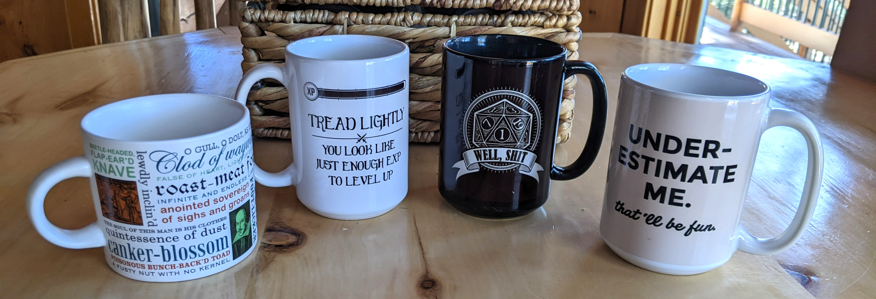 Four coffee mugs including a Shakespeare insult mug, two D&D related mugs, and one that just says “Underestimate me. That'll be fun.“