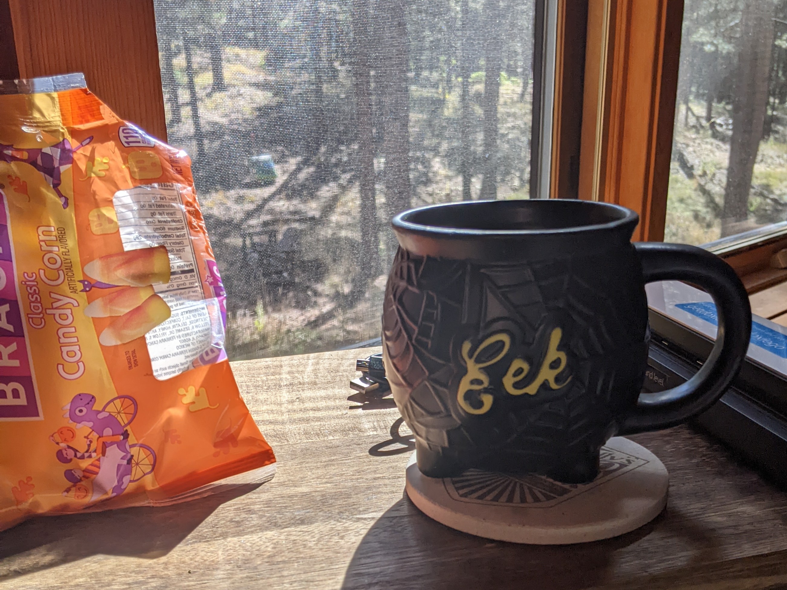 A picture of a bag of candy corn next to a coffee mug that looks like a cauldron.