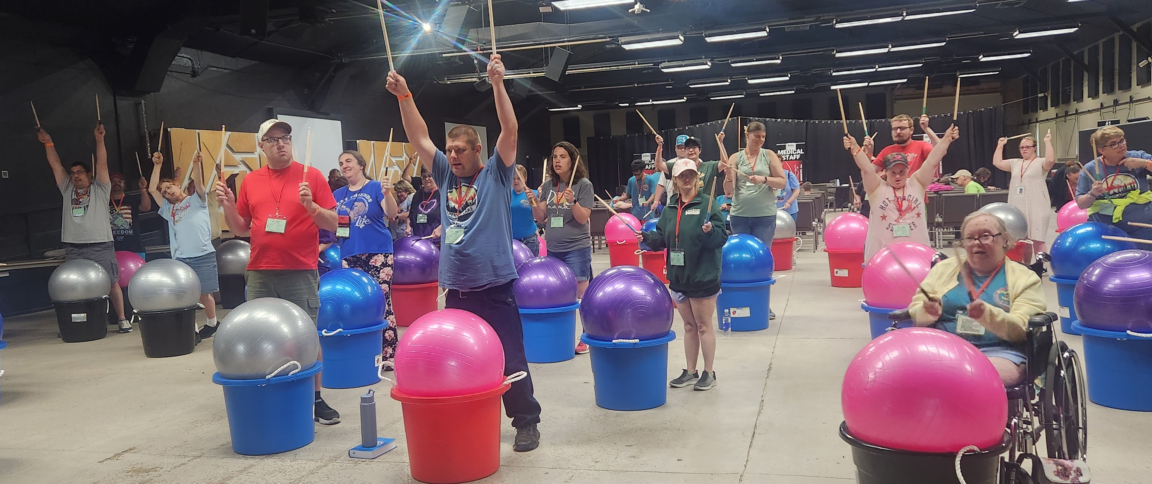 A number of people using sticks, large balls, and plastic dubs to drum