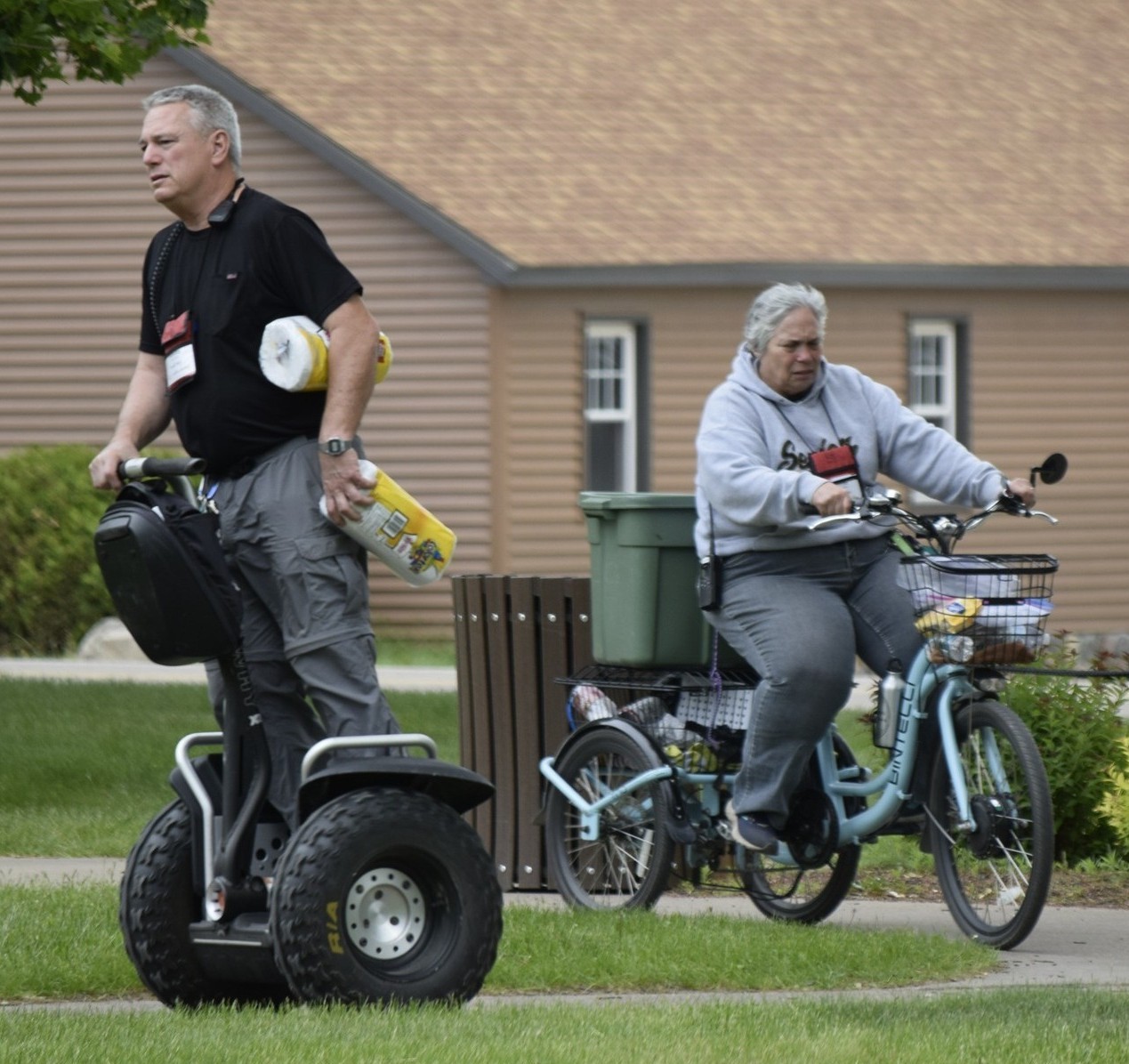ommy and Cindy Maher riding a self-balancing electric scooter (Segway) and a three-wheel bike while delivering equipment and supplies at camp.