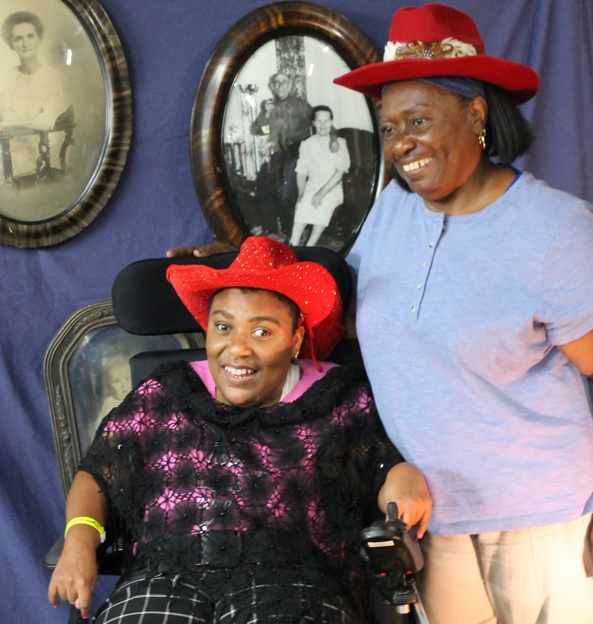 One woman standing another sitting in a wheelchair wearing red hats and posing for a fun western picture
