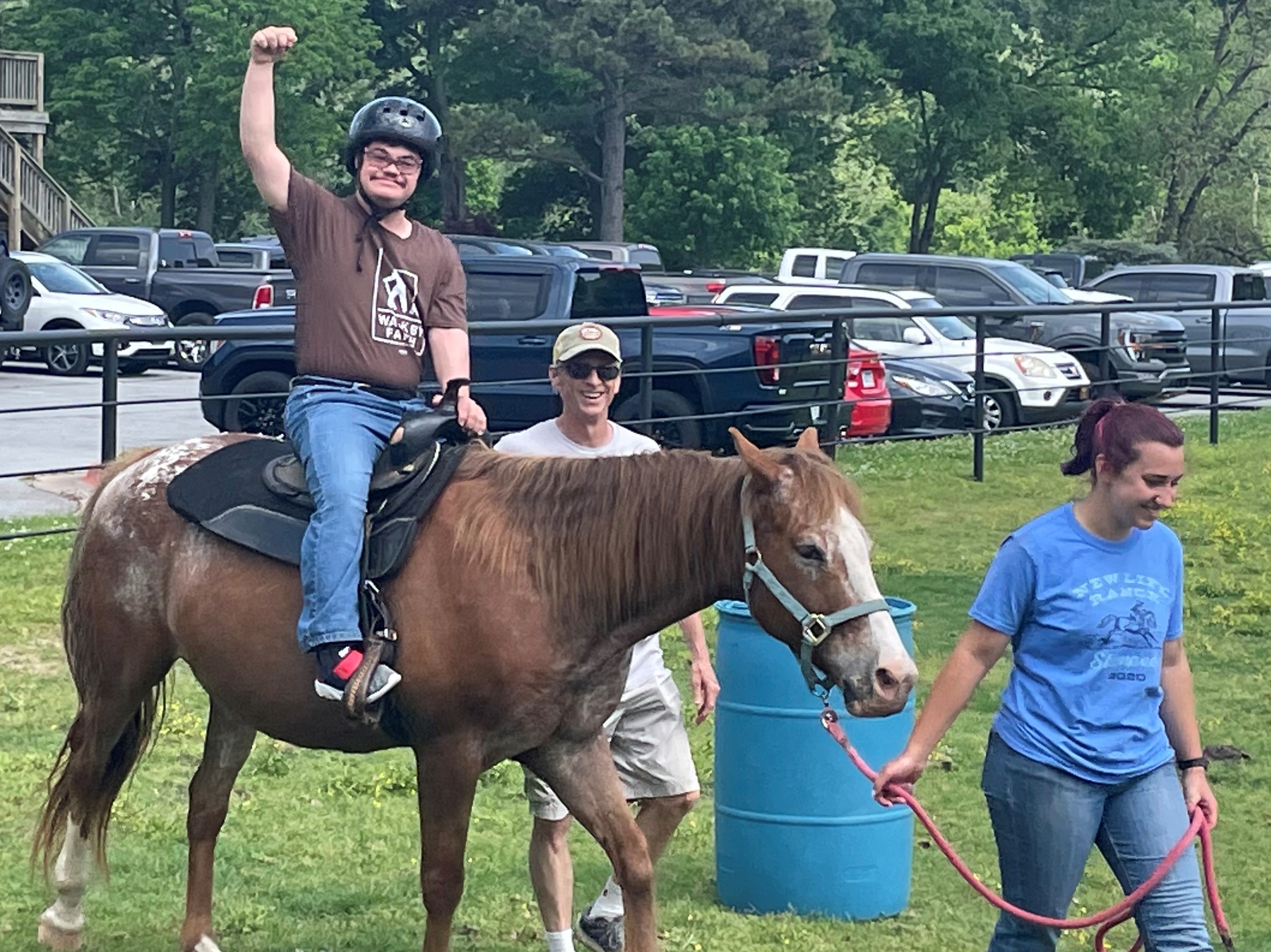 Man riding a horse with hand in the air with two people walking alongside.